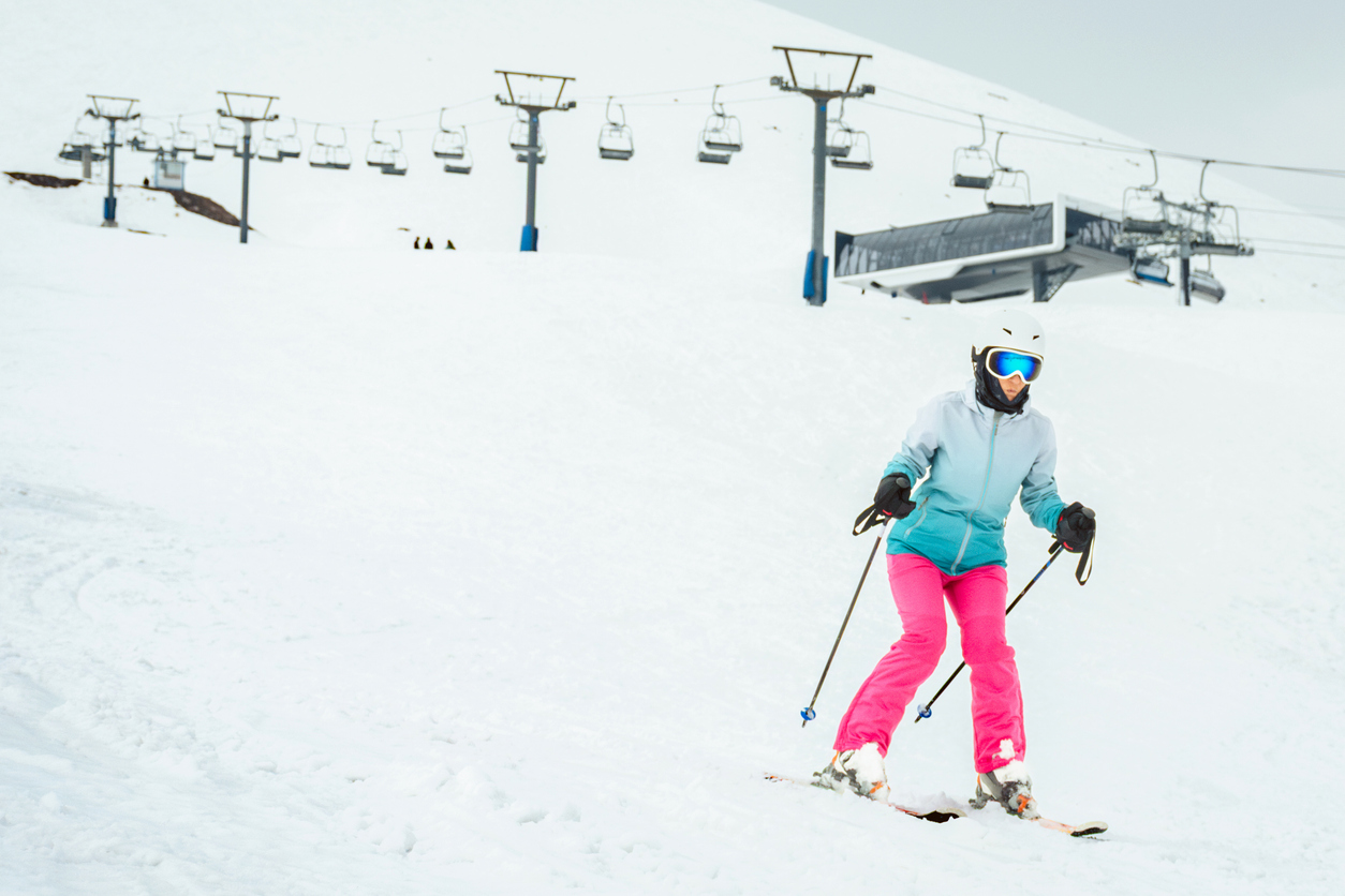 Woman skier in bright clothes skiing slowly on beginner slope with ski lift and station in Gudauri ski resort, Georgia Caucasus mountains